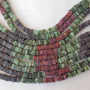 May include: A strand of dark gray, green, and red gemstone beads. The beads are rectangular and have a polished finish.