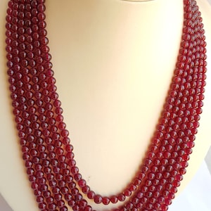 Op de afbeelding: Een meerstrengige ketting gemaakt van diep rode edelsteen kralen. De ketting is gemaakt van vijf strengen ronde kralen, elke streng is ongeveer 46 cm lang.
