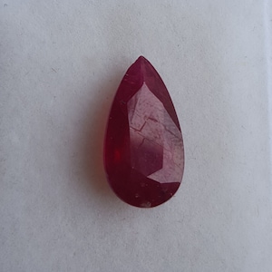May include: A deep red pear-shaped gemstone with a faceted cut.