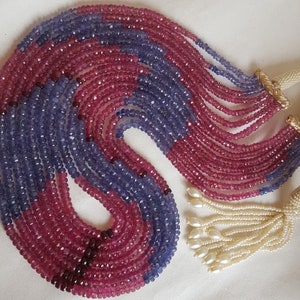 May include: A multi-strand necklace made of purple and pink gemstone beads. The necklace has a white pearl tassel.