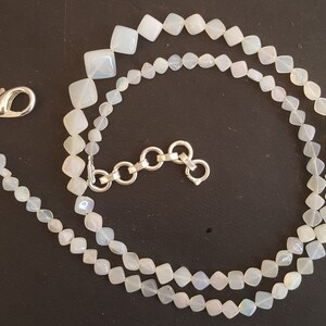 May include: A white opal necklace with a silver chain clasp. The necklace is made of square-shaped beads.