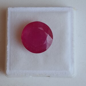 May include: A round, pink gemstone in a white box. The gemstone is faceted and has a smooth, polished surface.