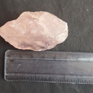 Peut inclure: Un gros cristal de quartz rose brut mesurant environ 5 cm de long. Le cristal est translucide et a une teinte rose clair.