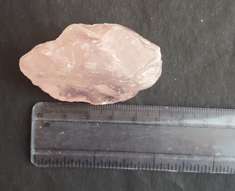 Peut inclure: Un gros cristal de quartz rose brut mesurant environ 5 cm de long. Le cristal est translucide et a une teinte rose clair.