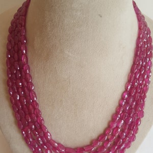 Op de afbeelding: Een meerrijige ketting gemaakt van roze ovale edelstenen. De ketting is gemaakt van vier rijen kralen en wordt getoond op een mannequin.