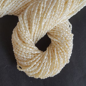 May include: A strand of off-white pearl beads, arranged in a circle on a black background.