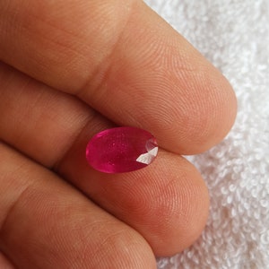 以下が含まれることがあります： 深紅色の鮮やかなオーバル型のルビーの宝石。宝石はファセットカットされており、研磨仕上げが施されています。