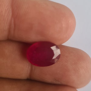 May include: A deep red oval gemstone with a faceted cut.