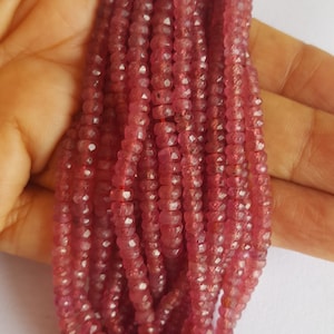 May include: A strand of pink ruby beads, faceted and with a slightly irregular shape. The beads are strung on a clear thread and are approximately 4mm in diameter.