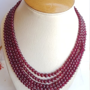 May include: A multi-strand necklace made of deep red gemstone beads. The necklace is displayed on a white mannequin bust.