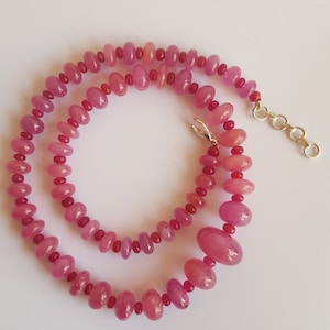 Puede incluir: Un collar de piedras preciosas rosas con cuentas de forma ovalada. El collar está hecho de una sola hebra de cuentas y tiene un cierre de plata.