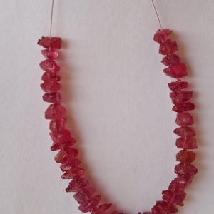 Könnte beinhalten: Eine Kette aus rosafarbenen Rubin-Edelsteinen, jede Perle ist facettiert und unregelmäßig geformt. Die Perlen sind auf einem dünnen Draht aufgefädelt.