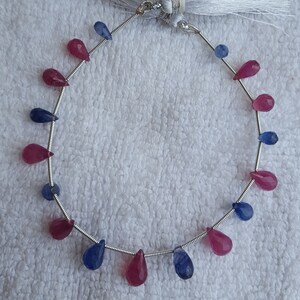 May include: A strand of gemstone beads, alternating between pink and blue teardrop-shaped beads. The beads are strung on a silver wire.