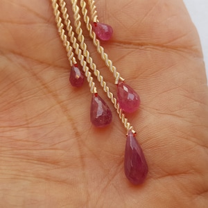 Peut inclure: Une chaîne dorée avec cinq pierres précieuses en forme de goutte rose qui pendent. La chaîne est torsadée et les pierres précieuses sont facettées.