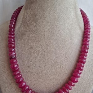 Op de afbeelding: Een ketting gemaakt van roze robijn kralen. De kralen zijn rond en hebben een gladde, gepolijste afwerking. De ketting wordt getoond op een mannequin.