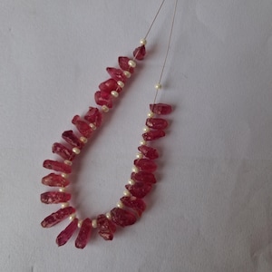 May include: A necklace made with pink ruby gemstone beads and white pearl beads. The beads are strung on a silver wire.