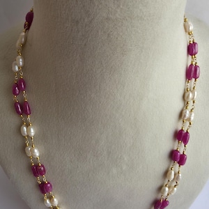 Op de afbeelding: Een dubbele ketting met afwisselende roze en witte kralen. De ketting is gemaakt van een gouden ketting en heeft roze ovale kralen en witte ronde parels.