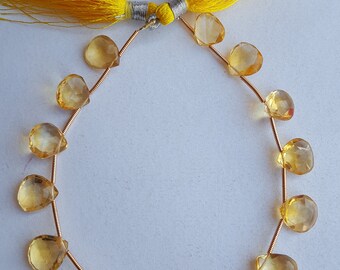 May include: A strand of 14 yellow citrine gemstone beads with faceted teardrop shapes. The beads are strung on a gold wire and have a yellow tassel on each end.