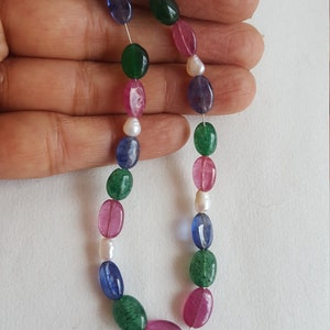 May include: A strand of oval-shaped gemstone beads in shades of green, blue, pink, and white. The beads are strung on a clear thread.