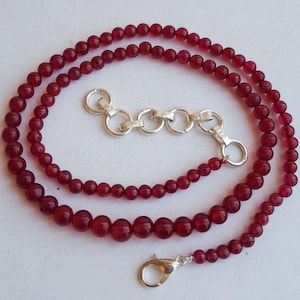 May include: A red gemstone necklace with a silver clasp and extender chain. The necklace is made of round beads and is approximately 18 inches long.