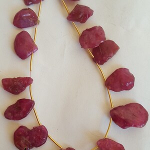 Puede incluir: Una hebra de cuentas de piedras preciosas rosadas enhebradas en un alambre dorado. Las cuentas tienen una forma irregular y una textura rugosa y natural.