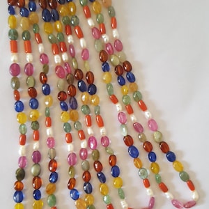 Puede incluir: Un collar de múltiples hilos con cuentas ovaladas en varios colores, incluyendo rojo, naranja, amarillo, verde, azul y rosa. Las cuentas están intercaladas con cuentas de perlas blancas y pequeñas cuentas rojas.
