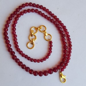 May include: A red gemstone beaded necklace with a gold clasp and extender chain. The necklace is made of small, round beads and has a simple, elegant design.