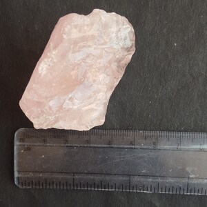 Peut inclure: Un grand cristal de quartz rose translucide avec une texture naturelle brute. Le cristal mesure environ 5 cm de long et 3 cm de large.