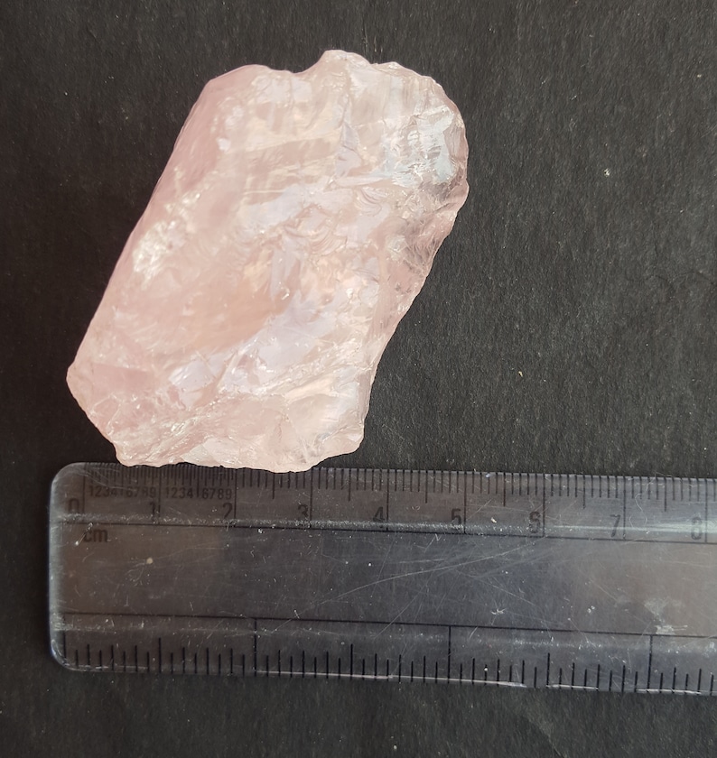 Peut inclure: Un grand cristal de quartz rose translucide avec une texture naturelle brute. Le cristal mesure environ 5 cm de long et 3 cm de large.
