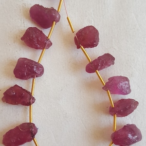 May include: A strand of pink gemstone beads strung on a gold wire. The beads are irregular in shape and have a rough, natural texture.