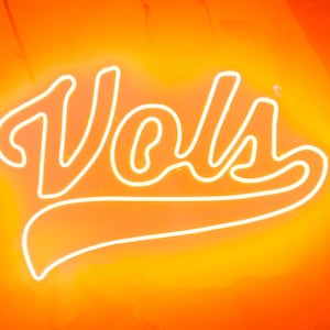 May include: A white neon sign with the word "VOLS" in a stylized font. The sign is on an orange background.
