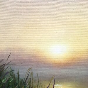 May include: A painting of a sunrise over a body of water with tall green grass in the foreground. The sun is a bright white circle in the center of the painting, and the sky is a soft yellow and pink.