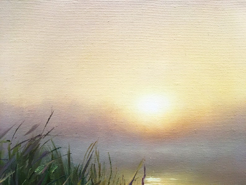 May include: A painting of a sunrise over a body of water with tall green grass in the foreground. The sun is a bright white circle in the center of the painting, and the sky is a soft yellow and pink.