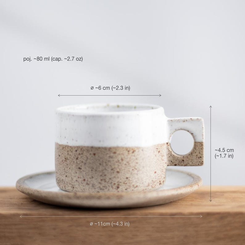 May include: A ceramic cup and saucer set with a speckled beige base and a smooth white upper section. The cup features a square handle with a circular cutout. Dimensions are 80 ml capacity, 2.3 inches in diameter, 1.7 inches in height, and 4.3 inches saucer.