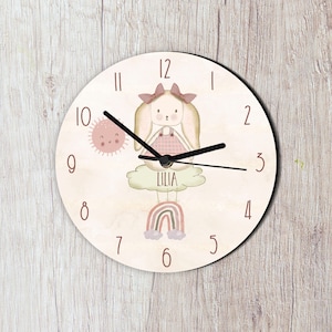 May include: A pink and white children's clock featuring a bunny rabbit illustration, a rainbow, and the name "Lilia" on the face.