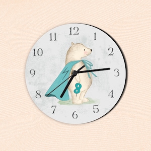 Pode incluir: Relógio de parede redondo com mostrador cinza claro com um urso de desenho animado usando uma capa azul com um raio. O urso está segurando o número 8. Os ponteiros pretos do relógio apontam para 2:15. Os números são pretos.