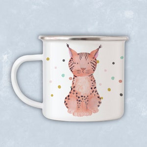May include: White enamel mug featuring a colourful illustration of a lynx sitting on a white background with gold, pink and blue polka dots.