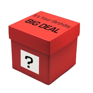May include: A square red gift box with a lid. The top of the lid features the black text "It's Your Birthday" and "BIG DEAL". A white square label with a black question mark is centred on the front side of the box, creating a mystery gift container.