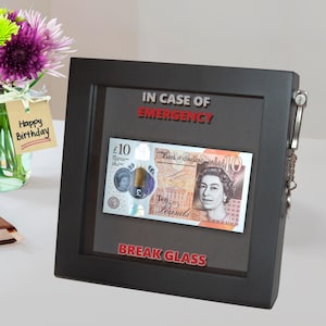 May include: A black framed box with a glass front that says "IN CASE OF EMERGENCY BREAK GLASS". Inside the box is a ten pound British banknote.