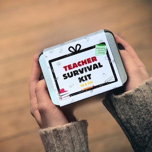 May include: A rectangular tin with a white label that reads "Teacher Survival Kit in a Tin" in red and black text. The label features illustrations of school supplies. The tin is held in two hands.