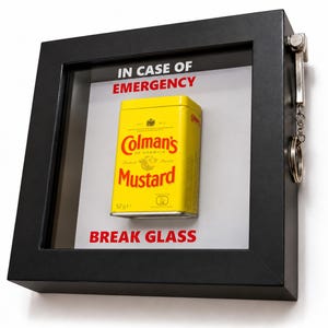 Puede incluir: Un marco cuadrado negro tipo vitrina que contiene una lata de mostaza amarilla Colman's. El fondo blanco presenta el texto rojo IN CASE OF EMERGENCY y BREAK GLASS. Un martillo de metal plateado está unido al lado derecho del marco.