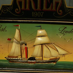 Peut inclure: Peinture nautique vintage représentant un bateau à vapeur avec des voiles et une roue à aubes. Le fond est vert et jaune, avec les inscriptions "Est. London" et "1907". Le tableau est encadré en noir.