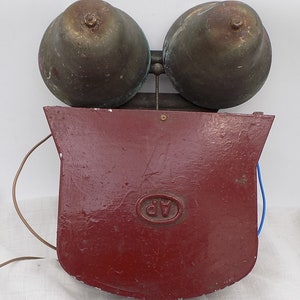 Könnte beinhalten: Ein antiker roter Feueralarm aus Metall mit zwei Messingglocken. Der Alarm hat ein rundes Etikett mit den Buchstaben "AP" in der Mitte.