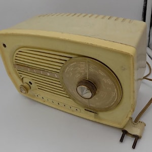 Könnte beinhalten: Ein cremefarbenes Philips-Radio im Vintage-Stil mit einem schwarzen Zifferblatt und einem silbernen Knopf. Das Radio hat eine Chromverkleidung und das Wort "Philips" ist auf der Vorderseite aufgedruckt.
