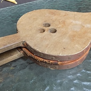 May include: A vintage wooden bellows with a leather and metal construction. The bellows has a rounded body with three circular holes and a long, tapered nozzle. A white strap is attached to the handle.