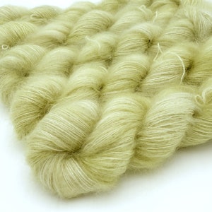 May include: Close-up of several skeins of soft, pale green yarn. The yarn has a fluffy, textured appearance with subtle white highlights. The skeins are arranged closely together, creating a dense, tactile surface. Ideal for knitting and crochet projects.