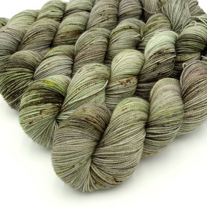 May include: A skein of yarn in shades of green, brown, and gray. The yarn has a speckled appearance, with small flecks of color throughout.