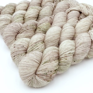 May include: A collection of yarn skeins in a neutral colour scheme. The yarn is a blend of light beige and grey, with small flecks of darker shades. The texture is visible, indicating a soft, natural fibre. Suitable for knitting and crochet projects.