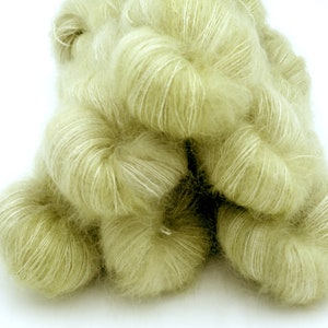 May include: A pile of soft, pale green yarn with a fluffy texture. The yarn appears to be a blend of fibers, with a subtle sheen and white highlights. Ideal for knitting or crocheting projects.