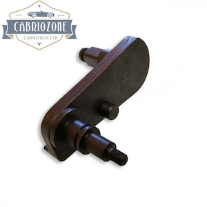 Puede incluir: Una pieza de coche de metal negro con dos pasadores de metal y un extremo roscado. La pieza está diseñada para ser utilizada en el mecanismo de capota convertible de un coche.